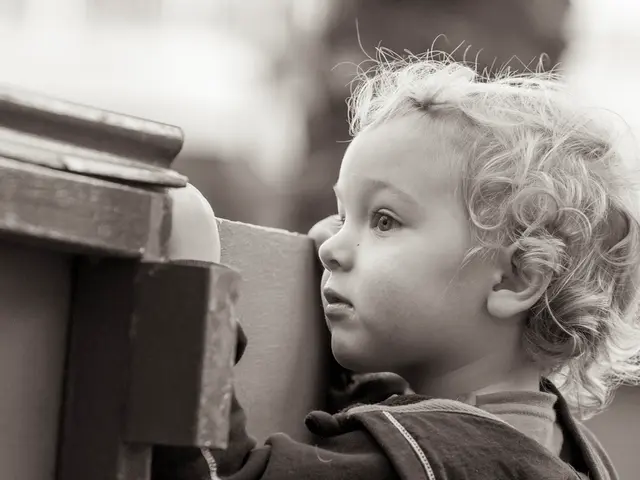 In this image we can see a kid standing near the wall and there are few objects beside the kid and...