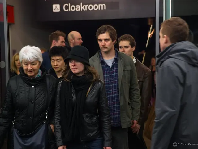 In the image there are many people in jackets standing and walking and behind them there is wall...