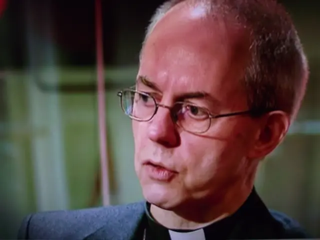 In the picture we can see a man with a bald head and some hair and he is in a black blazer.