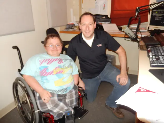 In this image there is a person sitting on the wheel chair , another person sitting on his knee,...