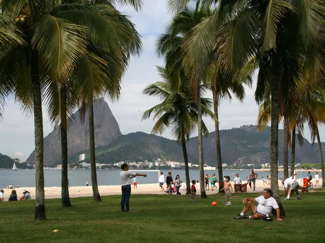 In this image there are people sitting on the grassland. There are people standing on the grassland...