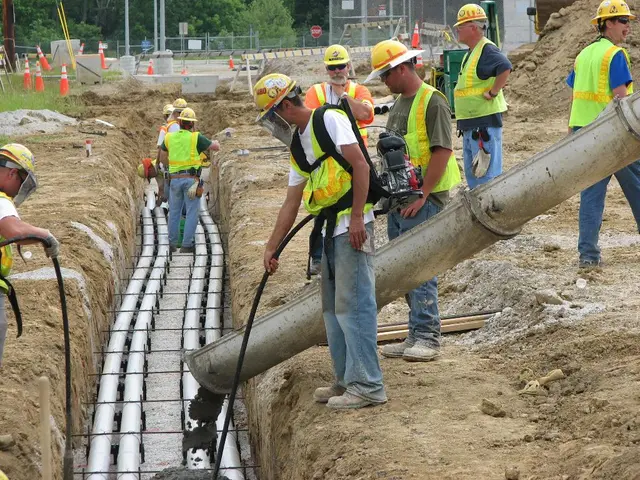 This image is taken at construction site. There are people wearing jackets and helmets. In the...