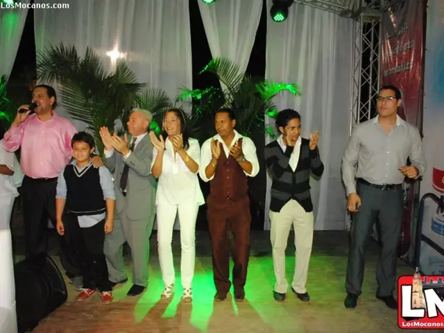 This image consists of some persons. Some of them are clapping. One is holding mic. There are pants...