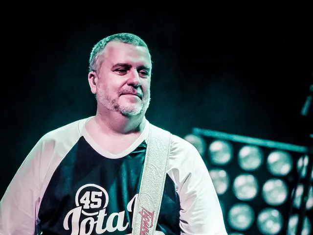 The person is standing and holding a guitar in his hands.