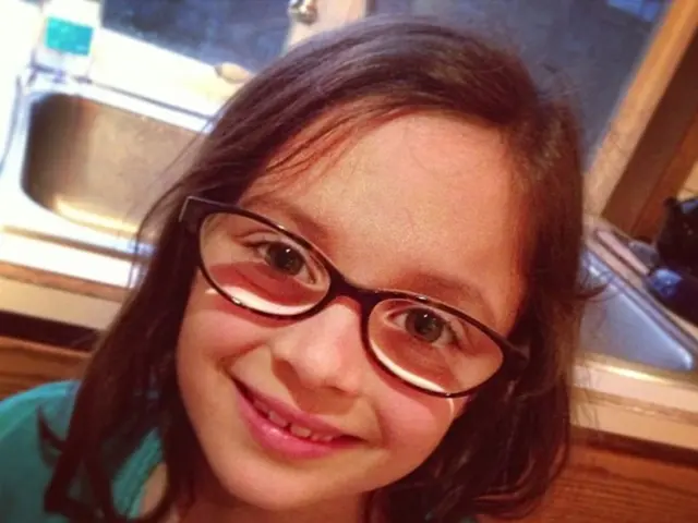 In this image we can see a child wearing spectacles. On the backside we can see a sink.