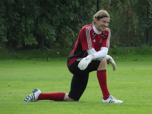 In the picture we can see a man sitting on the knee on the grass surface, the man is wearing a red...